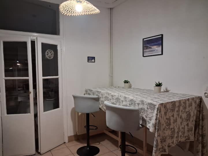 Petit coin repas avec nappe blanche, deux chaises, suspension lumineuse et porte vitrée la nuit
