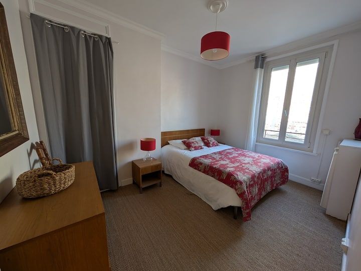 Chambre lumineuse avec un lit, des rideaux gris, une commode et une lumière naturelle.