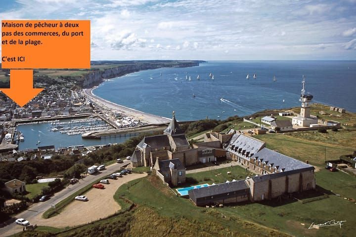 Vue de la ville portuaire et du littoral depuis un fort herbeux, avec une grande flèche indiquant la gauche.