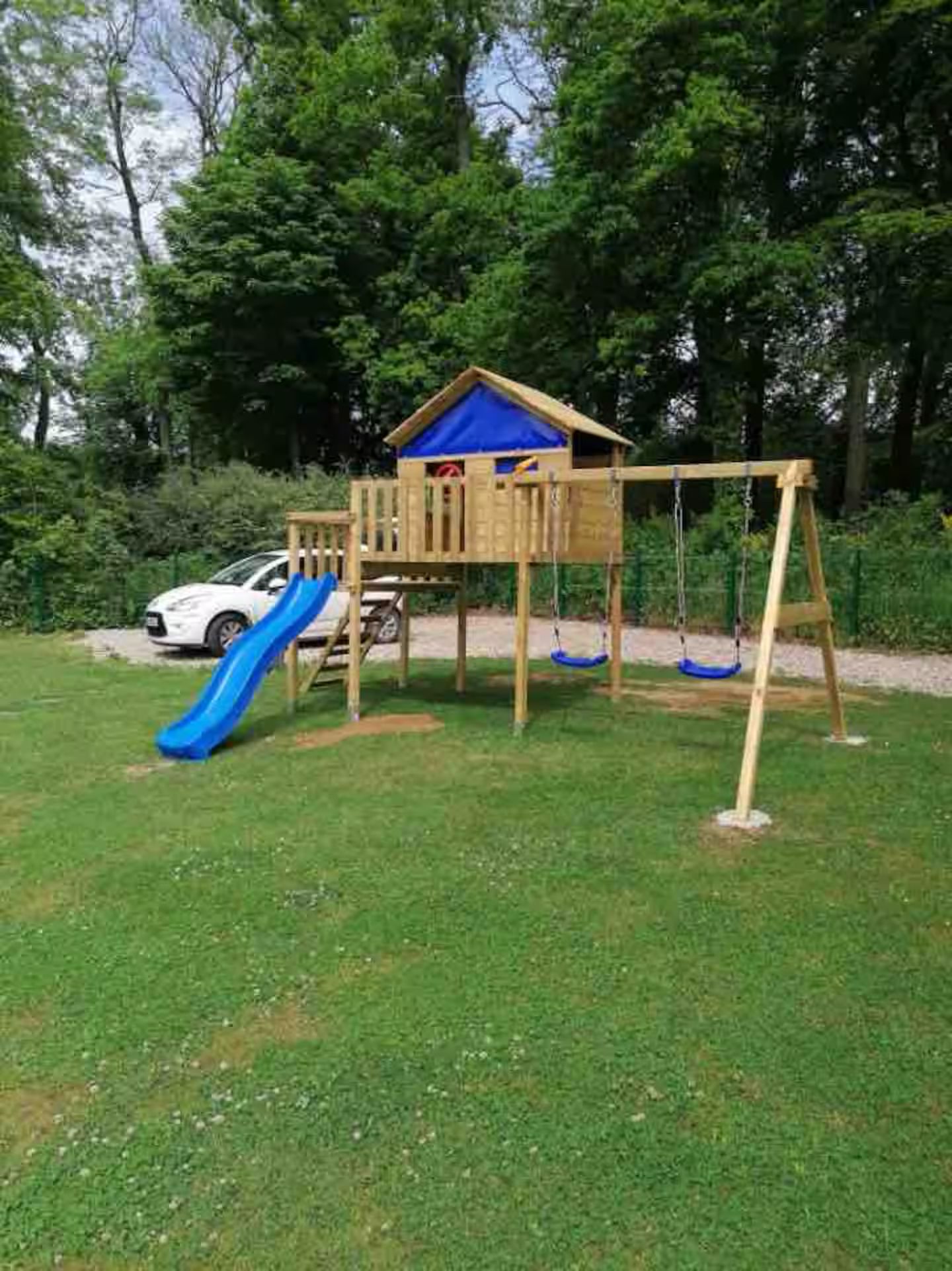 Une aire de jeux en bois avec un toboggan, des balançoires et une cabane dans les arbres.