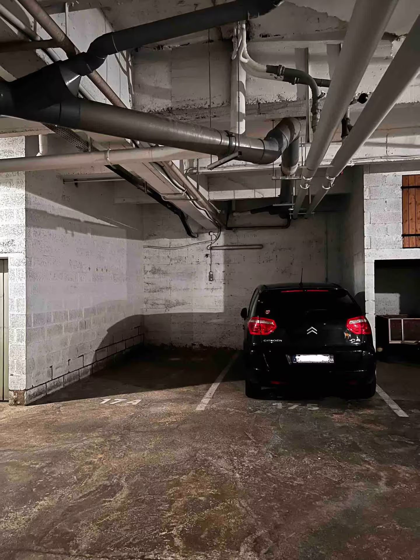 Une voiture est garée dans un parking avec des tuyaux suspendus au plafond.