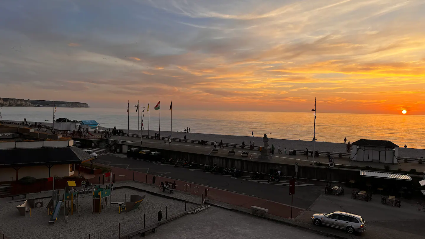 Une vue aérienne d'une plage au coucher du soleil avec des voitures garées sur le bord de la route.