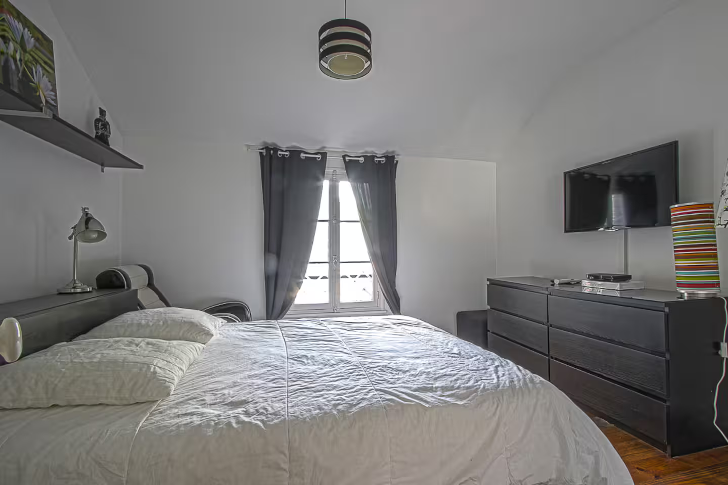 Une chambre avec un lit, une commode, une télévision et une fenêtre.