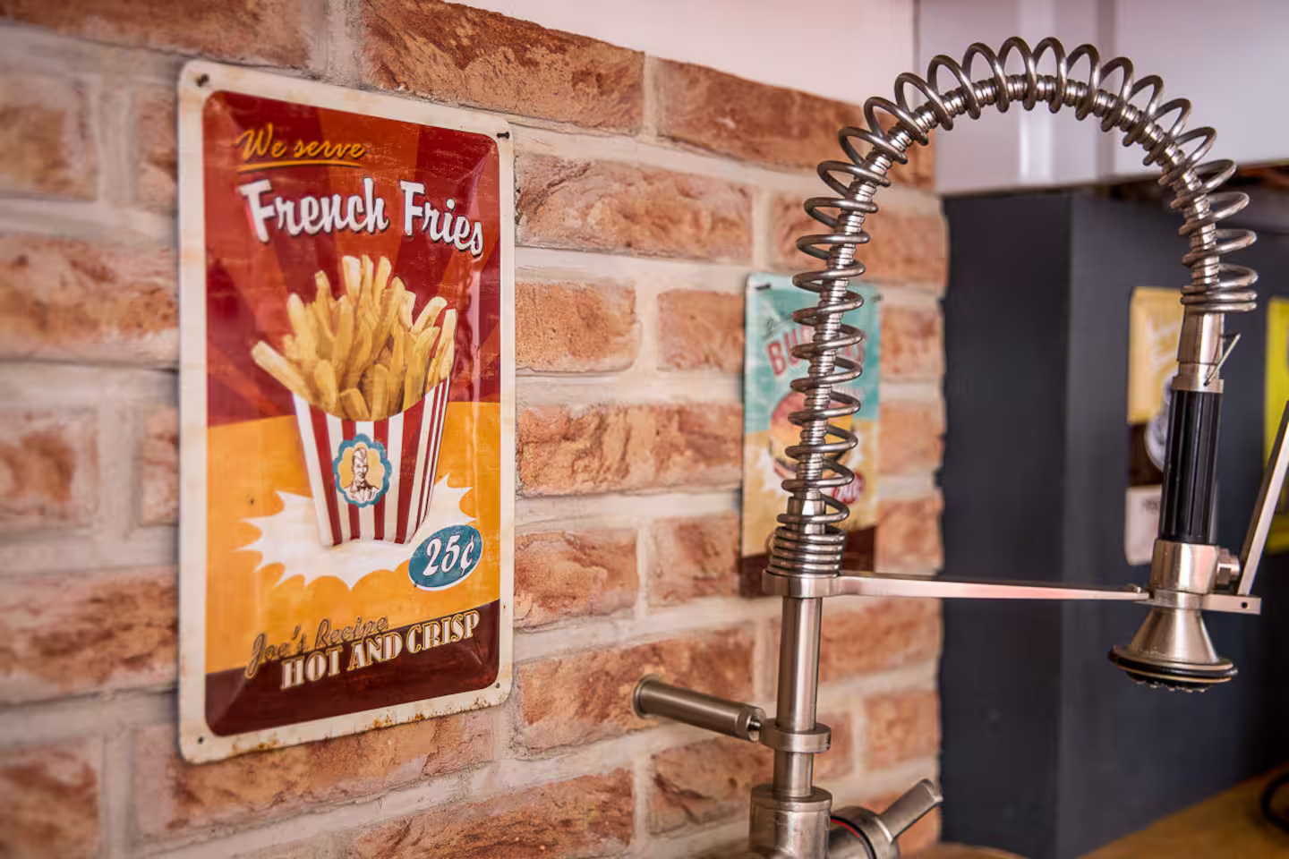 Un panneau pour des frites est accroché sur un mur de briques à côté d'un robinet.