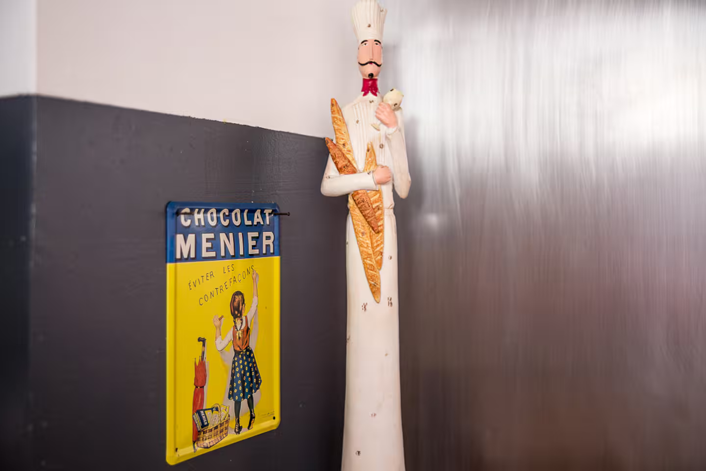 Une statue d'un chef tenant une miche de pain à côté d'un panneau.