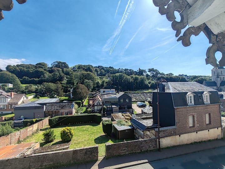 Vue d'une ville avec des maisons et de la verdure sous un ciel d'un bleu éclatant, depuis un point de vue élevé.