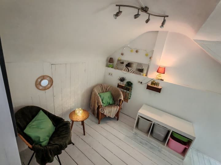 Coin lecture cosy sous les combles avec fauteuils, table d'appoint, rangements et étagères murales décoratives. Bois peint en blanc, touches de vert tendre.