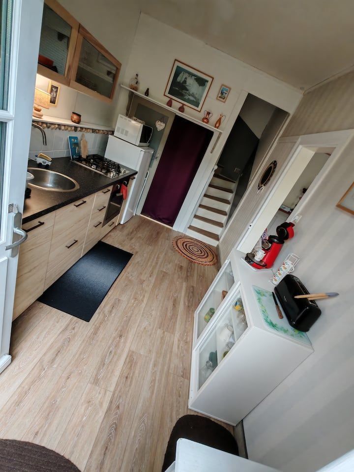 Petite cuisine avec placards et sol en bois clair, électroménager et escalier.