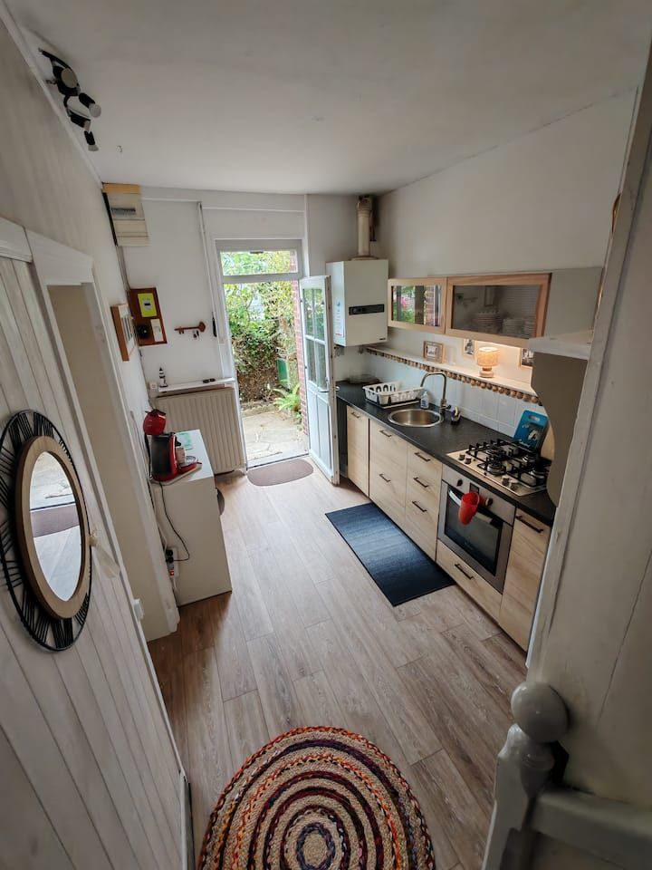 Cuisine étroite avec placards en bois, cuisinière, évier et porte donnant sur un petit espace extérieur.