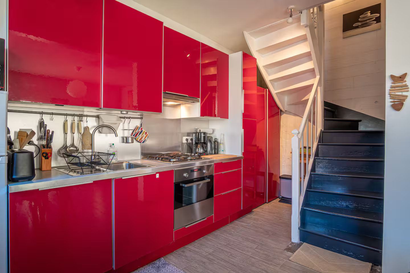 Une cuisine avec des armoires rouges et un escalier bleu menant au deuxième étage.