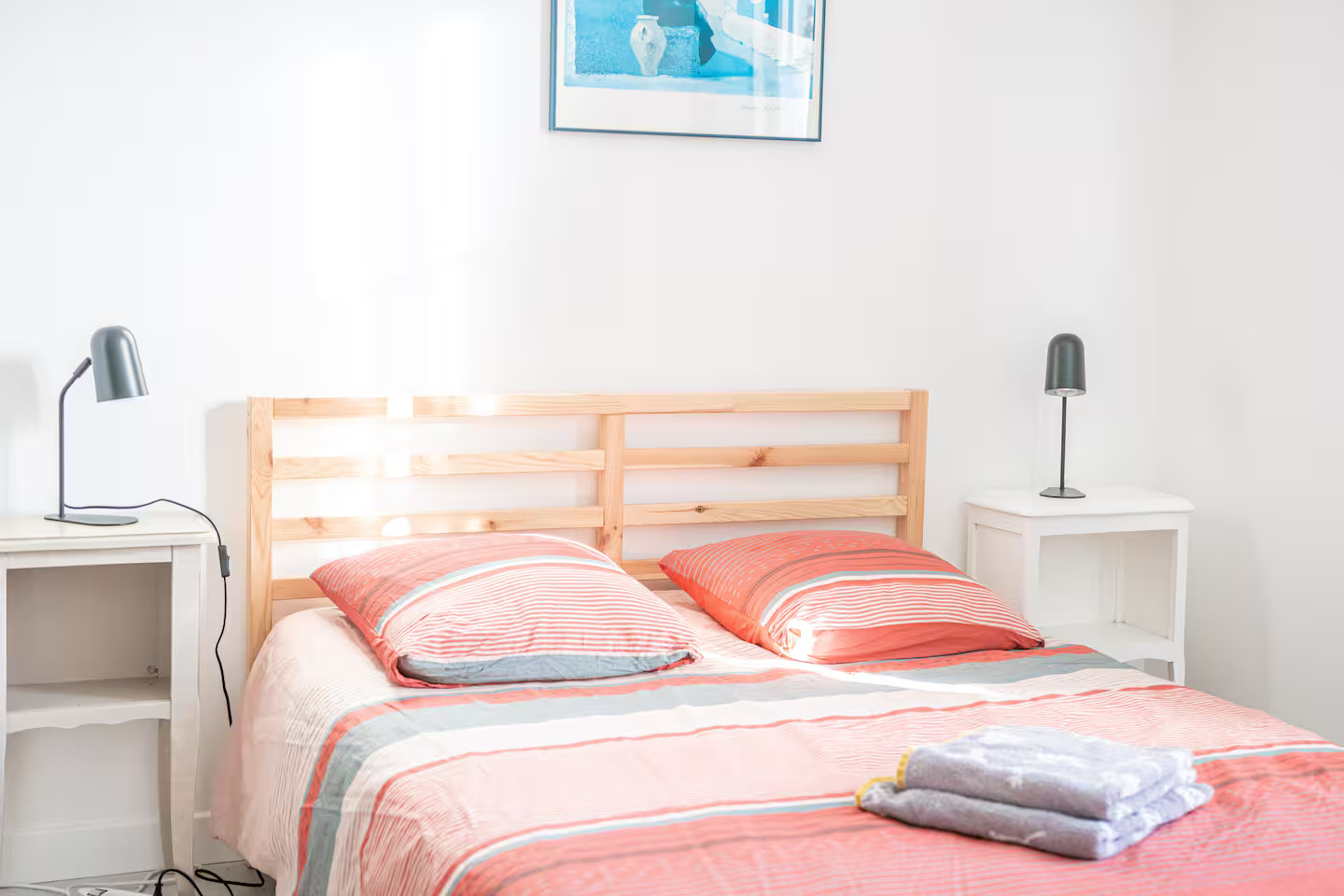 Une chambre avec un lit, deux tables de nuit, une lampe et un tableau au mur.