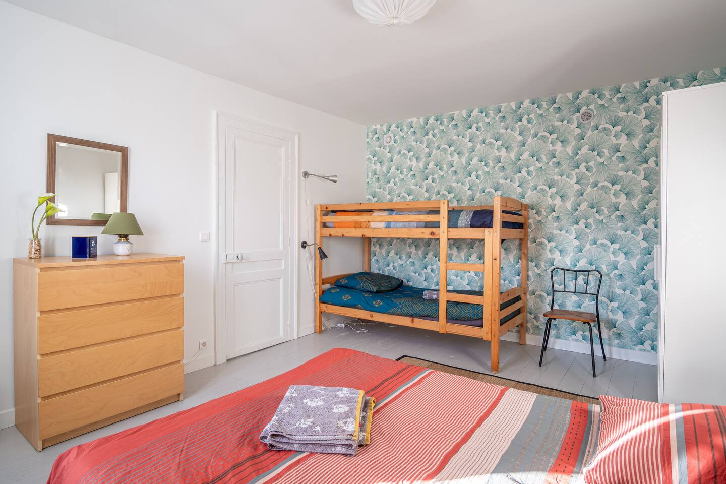 Une chambre avec un lit superposé, une commode, une chaise et un miroir.