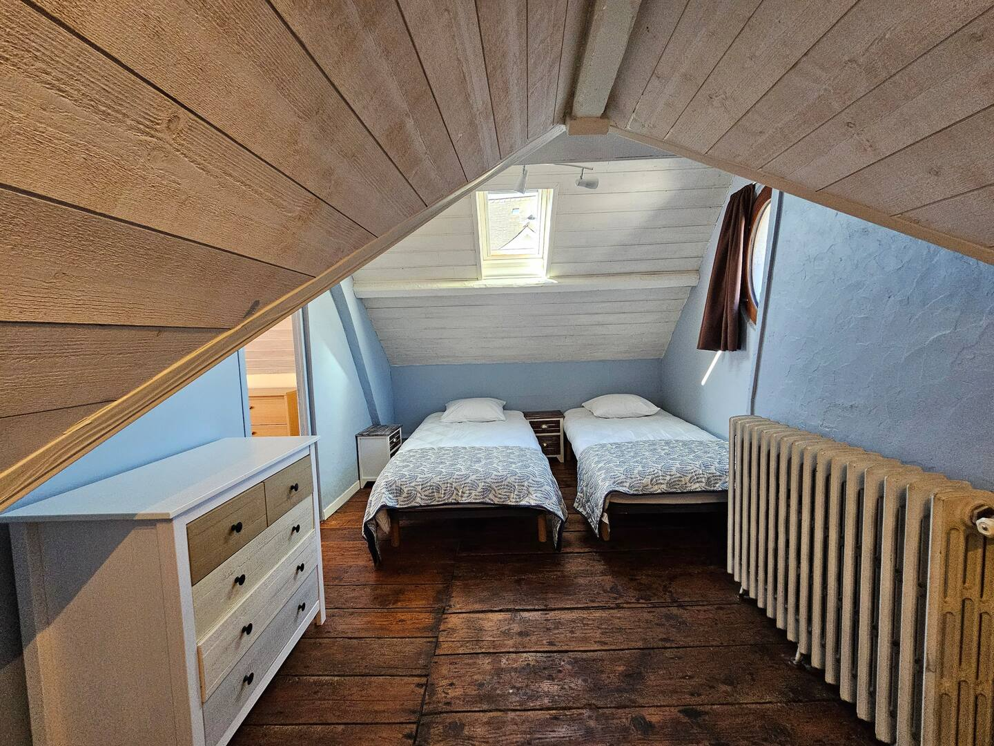Une chambre avec deux lits, une commode et un radiateur.