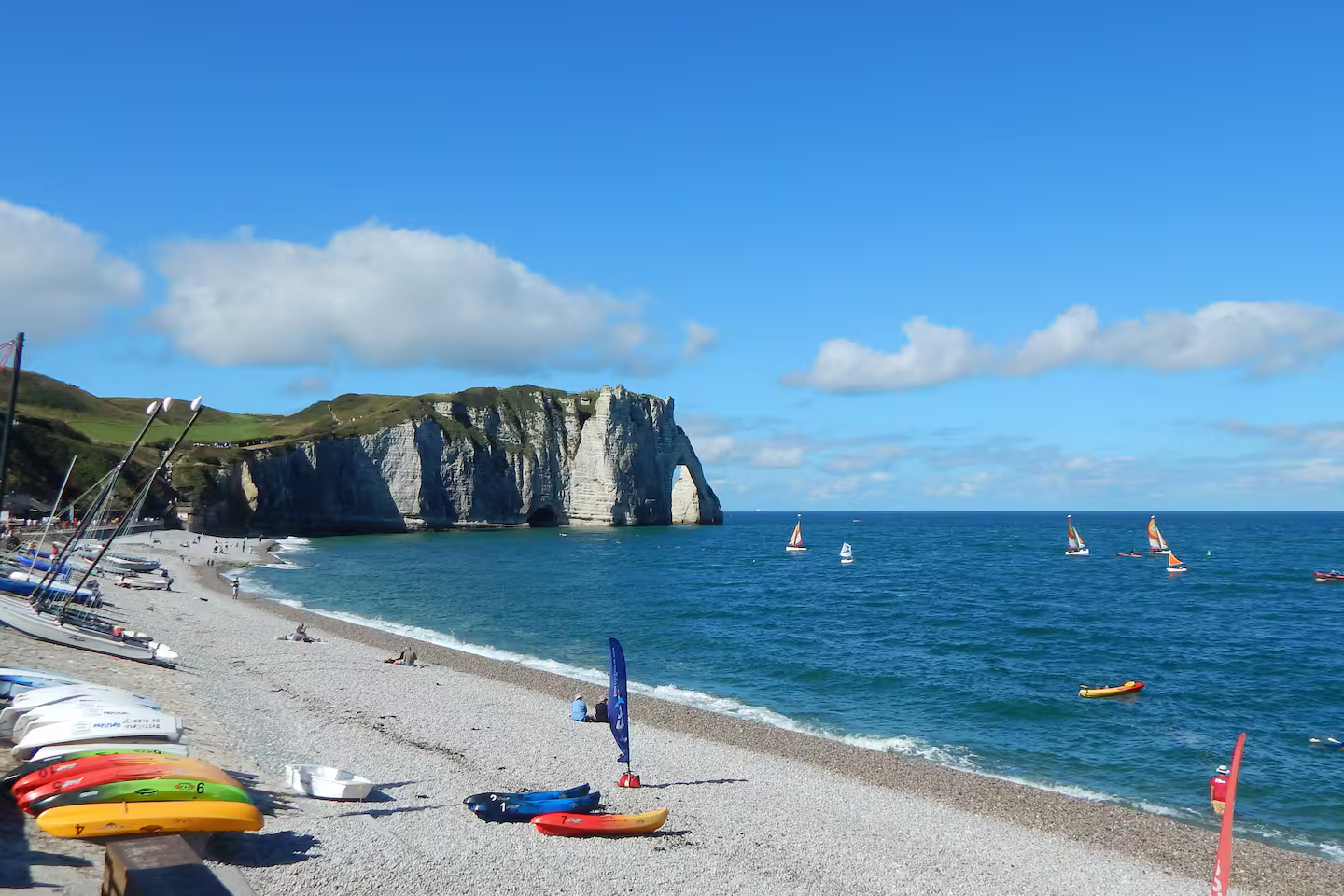 Une plage avec un gros rocher en arrière-plan et des bateaux dans l'eau