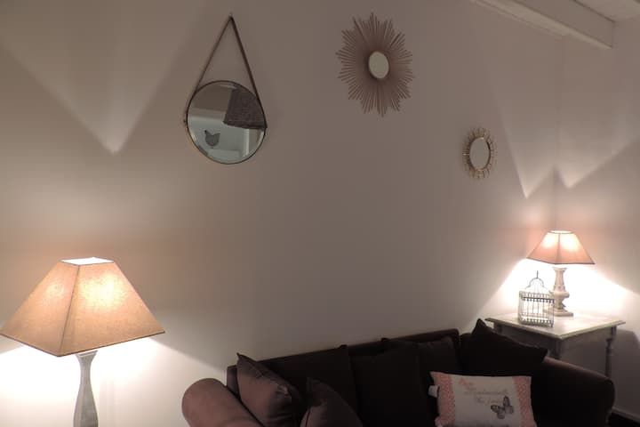 Salon cosy avec canapé marron, lampes et miroirs décoratifs sur un mur blanc.