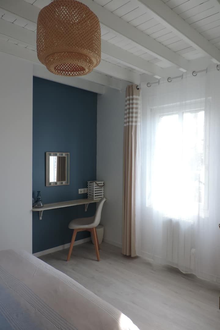 Chambre avec un mur d'accent bleu, un bureau, une fenêtre avec des rideaux transparents et une suspension lumineuse en tissu tressé.