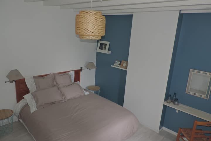 Chambre avec literie beige, mur d'accent bleu, éléments en bois et suspension en osier.