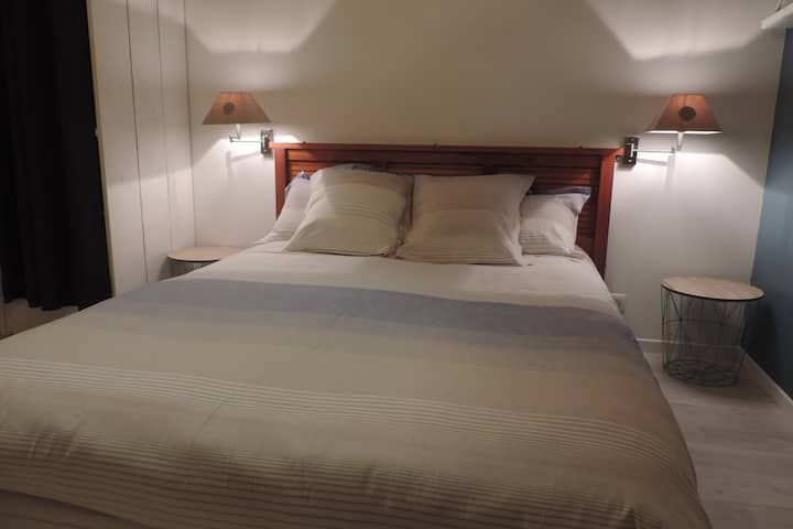 Chambre avec lit, tables de chevet, appliques murales et tête de lit en bois.