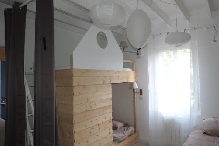 Lit superposé en bois avec un toit en forme de maison, dans une chambre blanche décorée de lanternes en papier et de voilages.