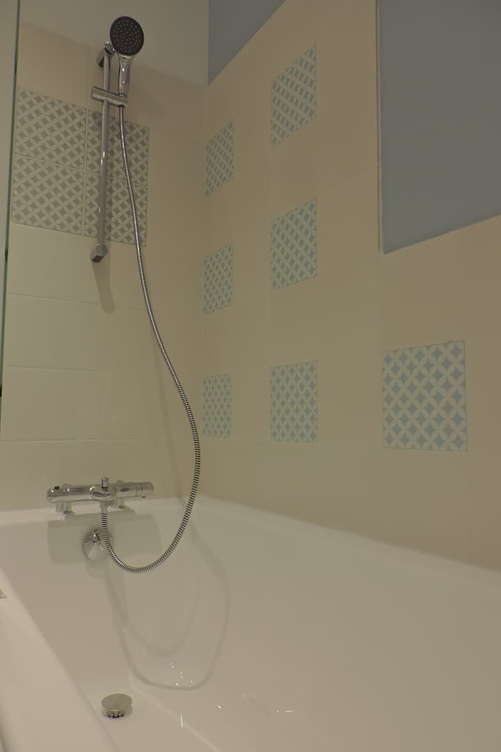 Baignoire blanche avec pommeau de douche et carrelage mural à motifs.