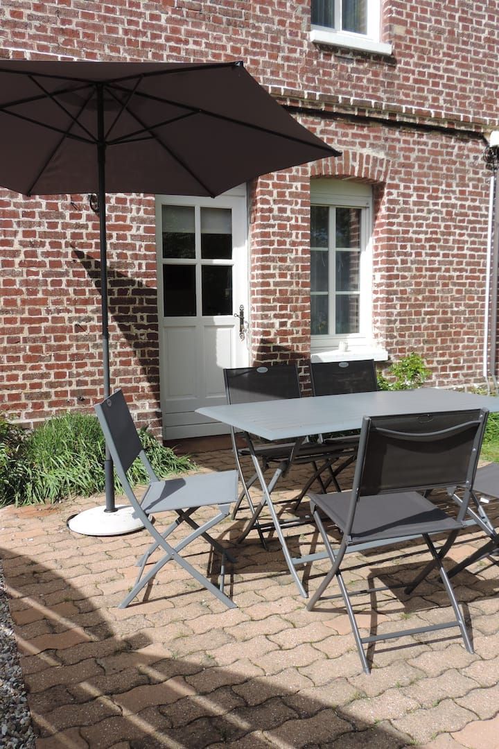 Terrasse avec table, chaises, parasol et bâtiment en briques avec porte et fenêtre blanches.