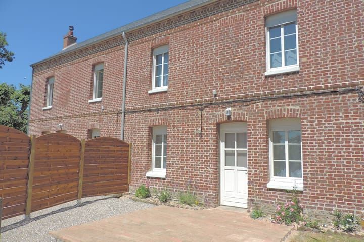 Bâtiment en briques rouges avec encadrements, porte et fenêtres blancs ; clôture en bois.