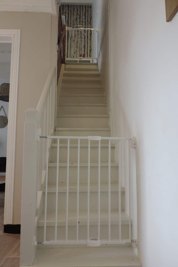 Escalier avec deux barrières de sécurité blanches, une en bas, une en haut. Murs et marches blancs.