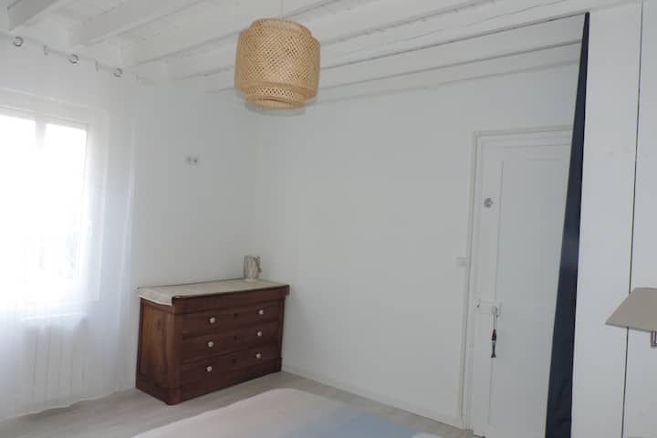 Chambre blanche lumineuse avec commode en bois, porte blanche et suspension lumineuse en tissu tressé.