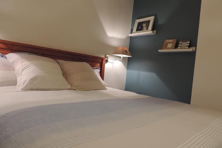 Lit avec draps blancs, oreillers et tête de lit en bois, près d'un mur d'accent bleu avec des étagères.