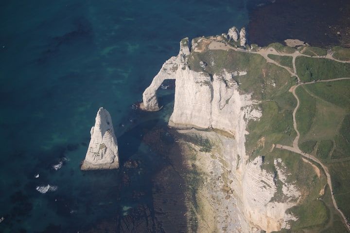 Falaises blanches avec une arche naturelle et un rocher isolé se détachant sur une eau bleu foncé, Normandie, France.