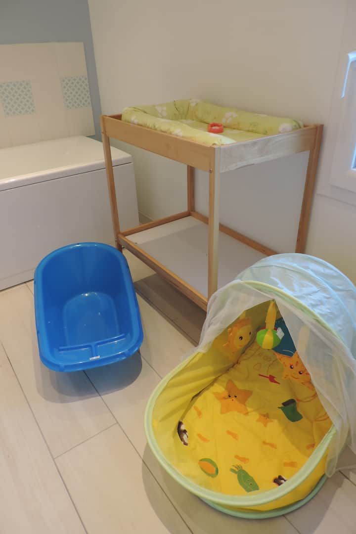 Une chambre avec tout le nécessaire pour bébé : une baignoire bleue, un tapis d’éveil jaune, une table à langer et un meuble de rangement blanc.