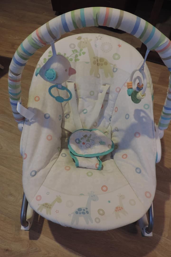 Transat pour bébé avec siège à motifs et jouets suspendus, avec une barre rayée au-dessus.