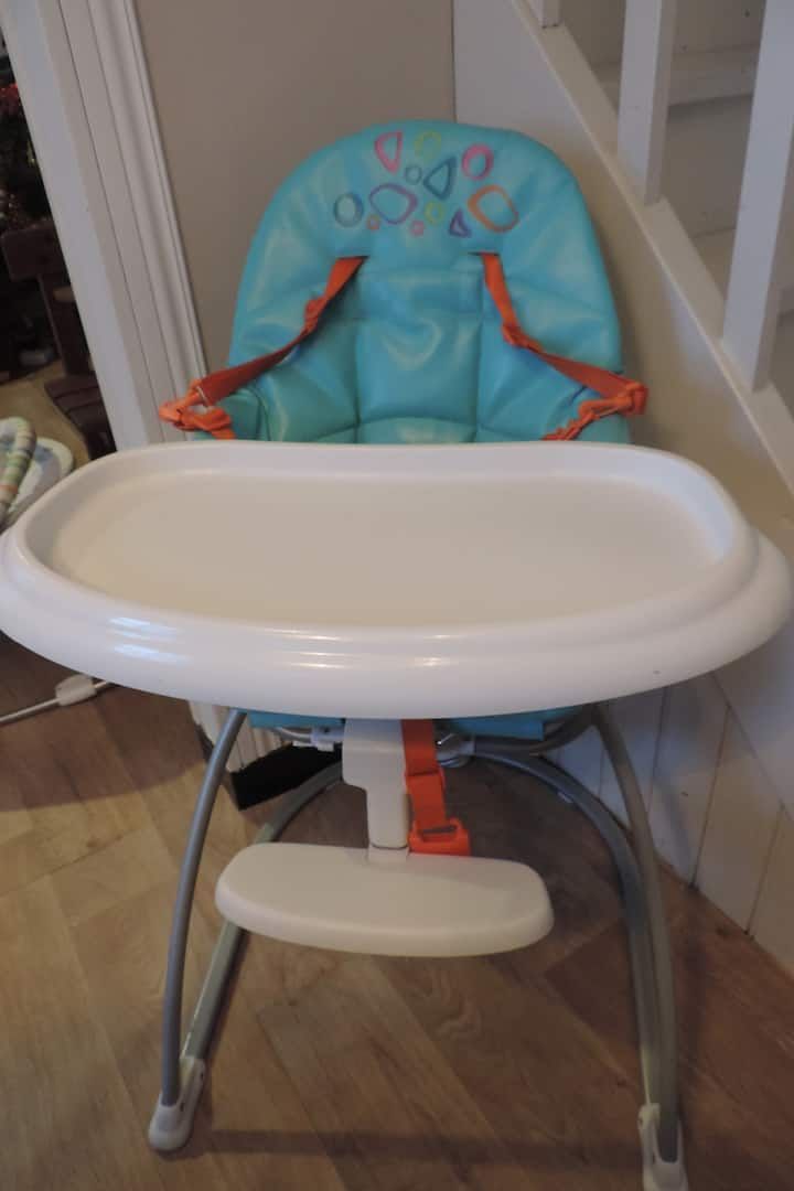 Chaise haute bébé bleue et blanche avec tablette et sangles de sécurité orange, pour l'intérieur.