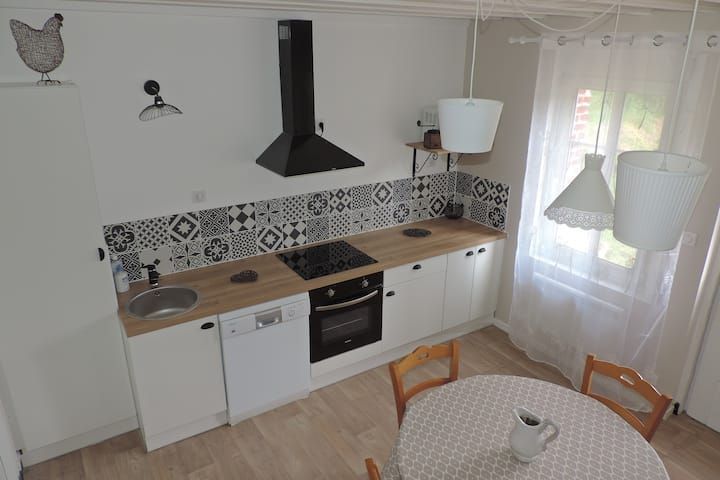 Cuisine lumineuse avec placards blancs, plan de travail en bois, crédence en carrelage noir et blanc et table à manger ronde.