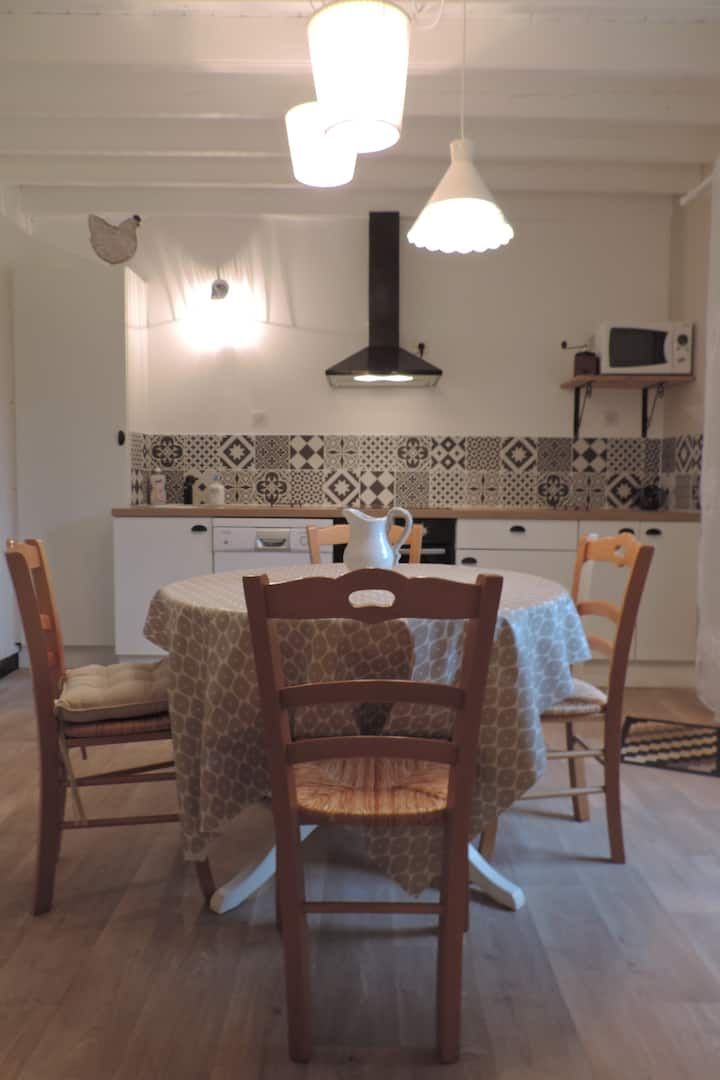 Cuisine avec placards blancs, table ronde pour quatre personnes, crédence à motifs et éclairage au plafond.