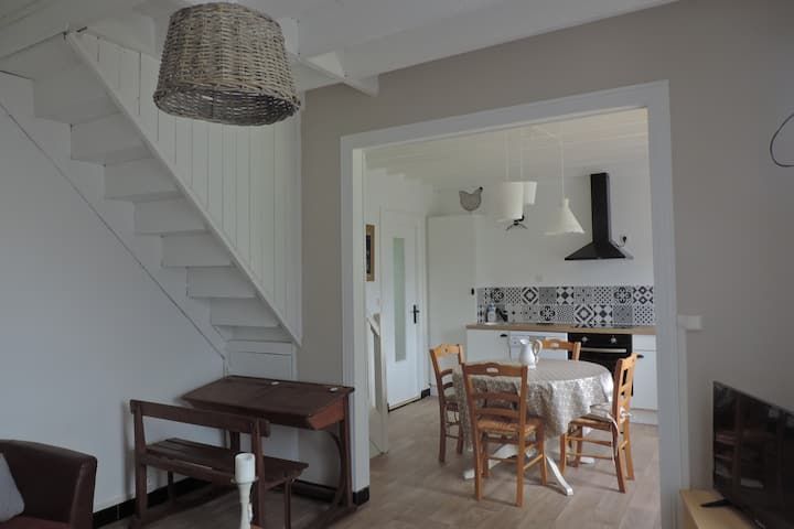Un intérieur chaleureux avec un escalier blanc, une cuisine et un coin repas comprenant une table ronde et des chaises en bois.