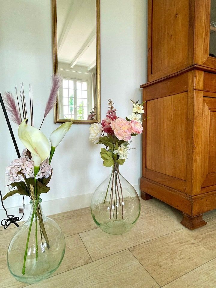 Deux vases en verre transparent contenant des fleurs sont placés devant un miroir et une armoire en bois.