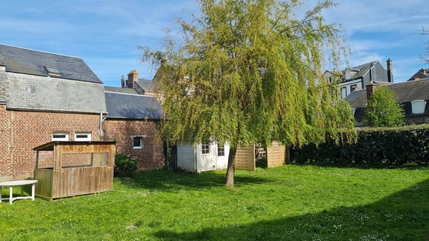 Une cour verdoyante avec un bâtiment en briques à l'arrière-plan et un arbre au premier plan.