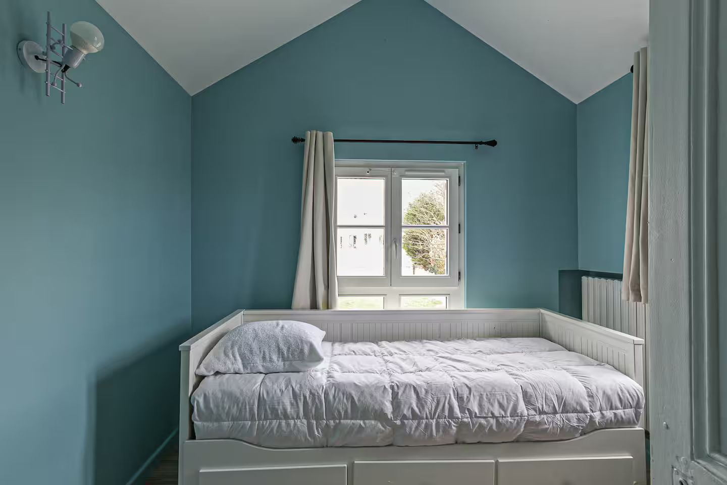 Une chambre avec des murs bleus et un lit de repos.