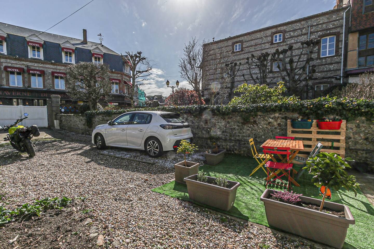 Une voiture blanche est garée dans une allée de gravier devant un bâtiment.