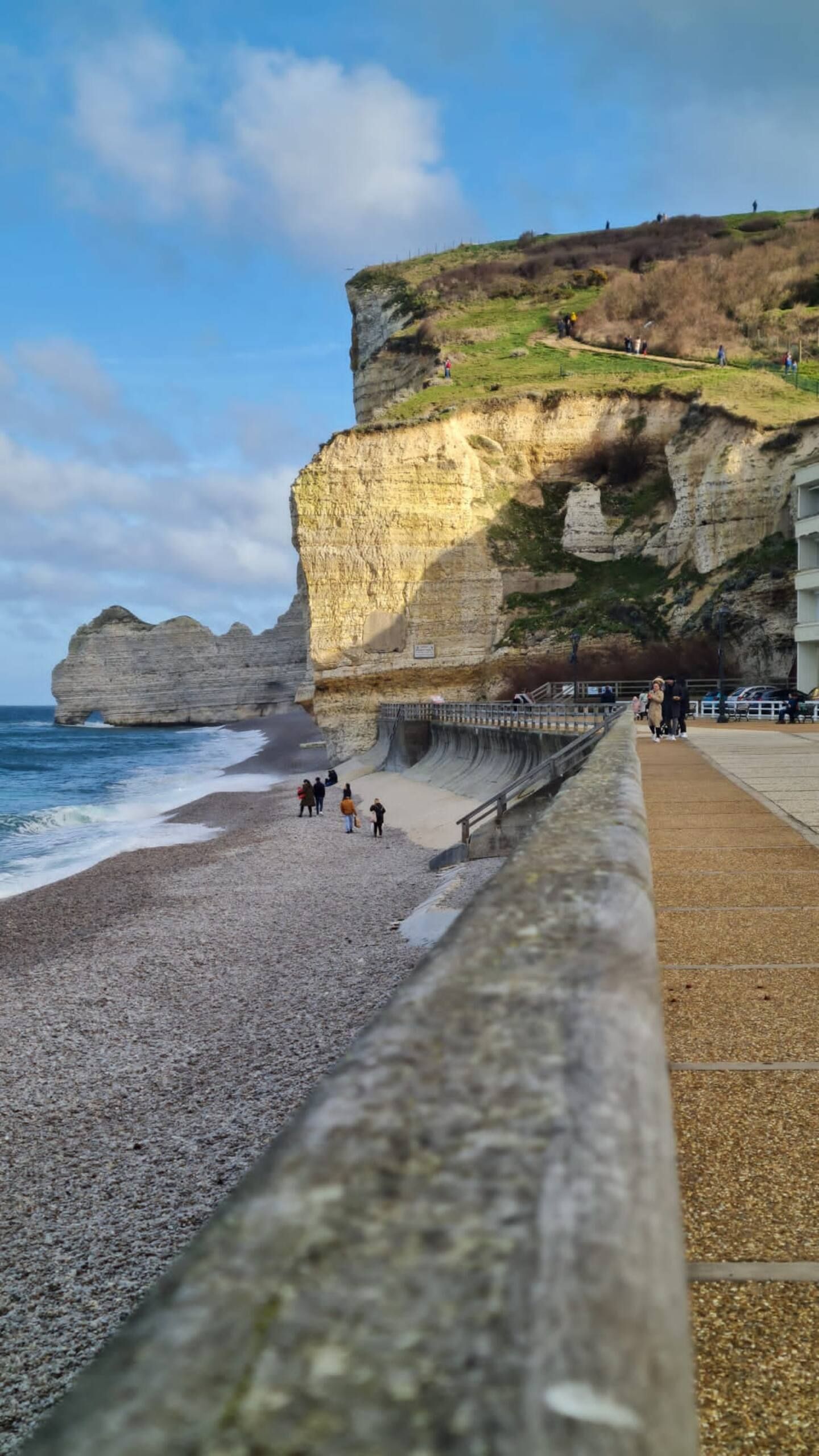 Une plage avec une falaise en arrière-plan et des gens marchant sur la plage.