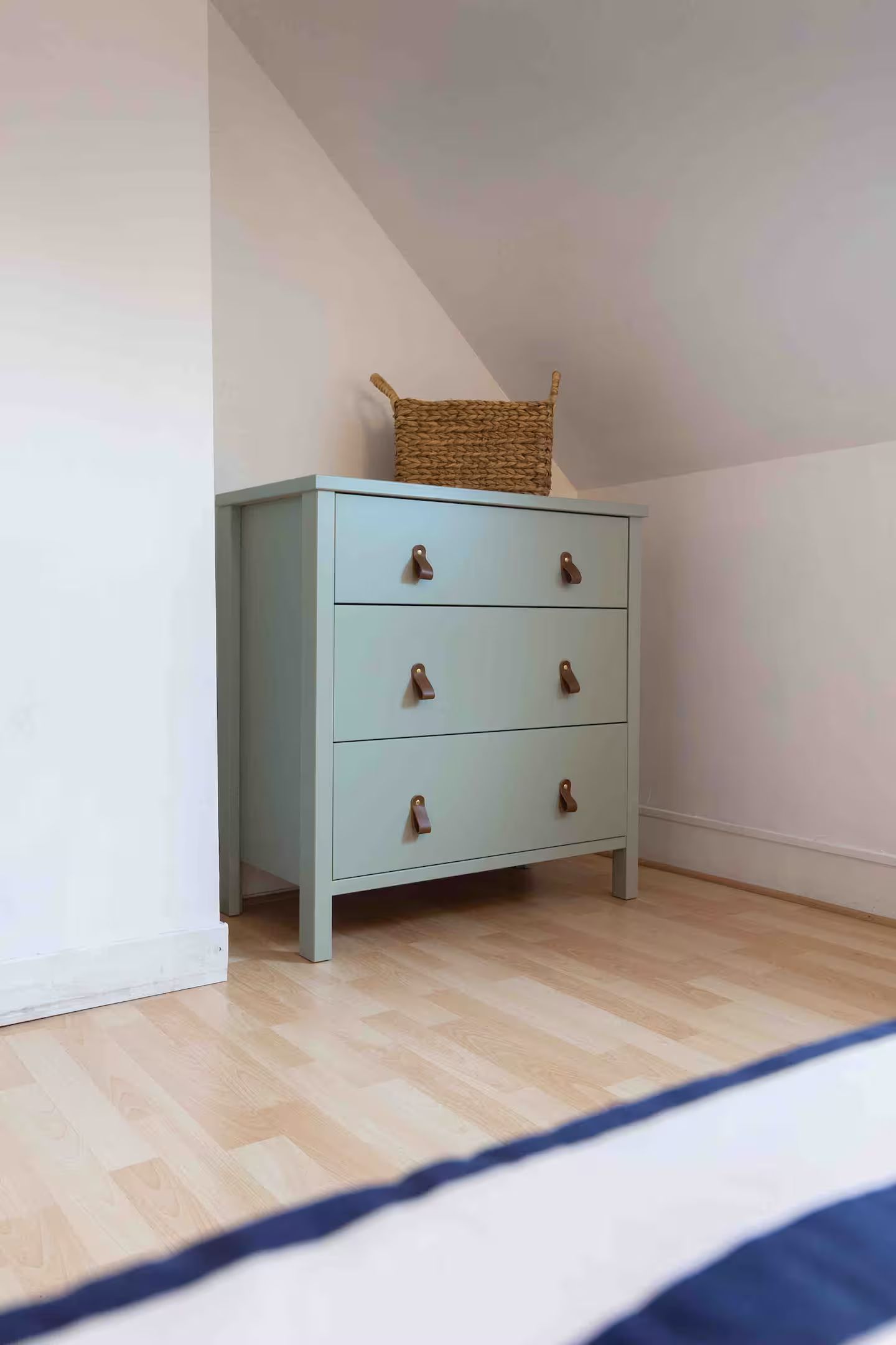 Une chambre avec une commode bleue et un panier dessus.