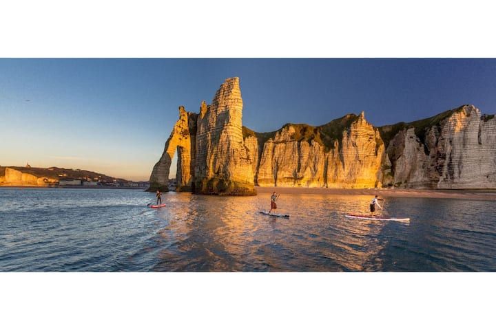Des pratiquants de paddleboard près des formations rocheuses emblématiques d'Étretat, en France, au coucher du soleil.