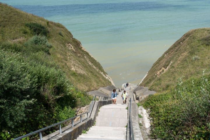 Escalier descendant une falaise herbeuse vers la mer, deux personnes descendent.