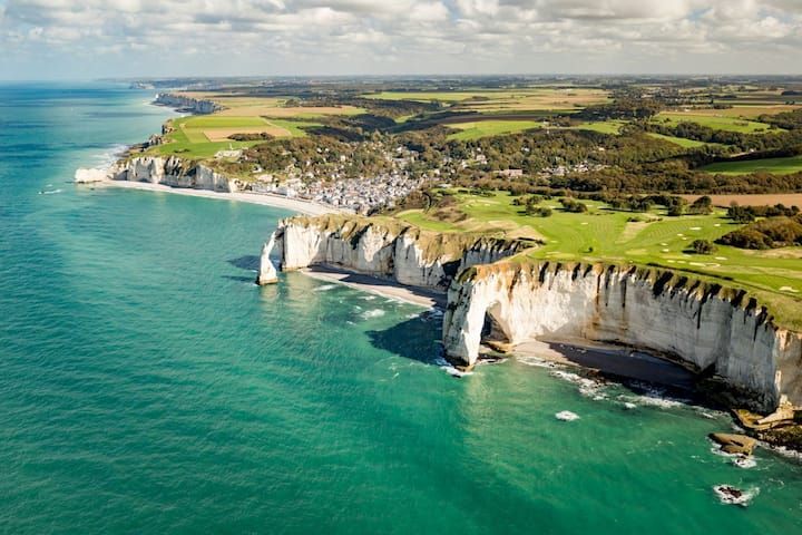 Falaises blanches surplombant une eau turquoise et une terre verdoyante sous un ciel partiellement nuageux.