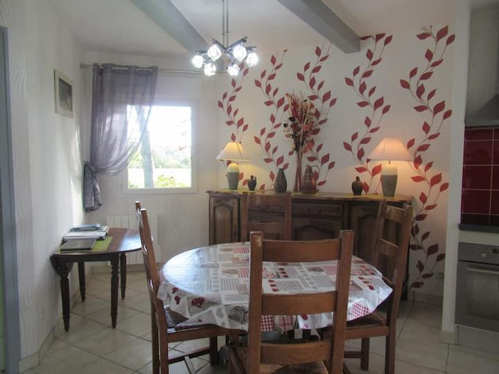 Salle à manger avec table ronde dressée pour un repas, buffet et mur d'accent orné d'un motif de feuilles rouges.