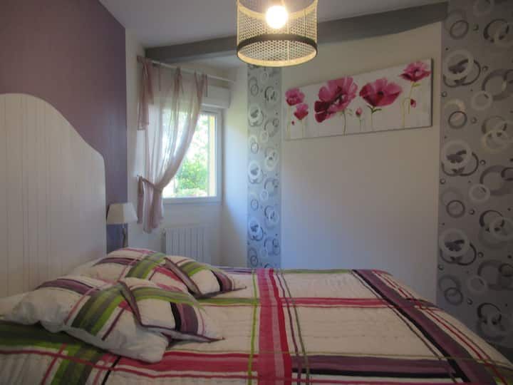 Chambre avec un lit, des murs violets, du linge de lit à motifs floraux et des œuvres d'art représentant des fleurs roses.