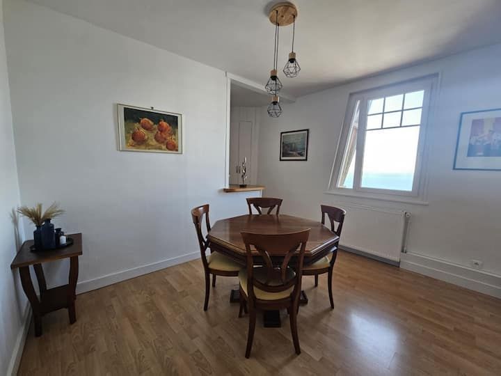 Salle à manger avec table et chaises en bois, parquet et fenêtre.
