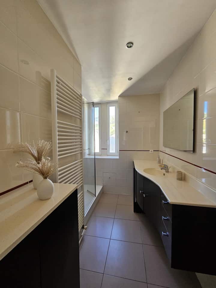 Salle de bains avec murs carrelés blancs, douche et meubles-lavabos en bois foncé.