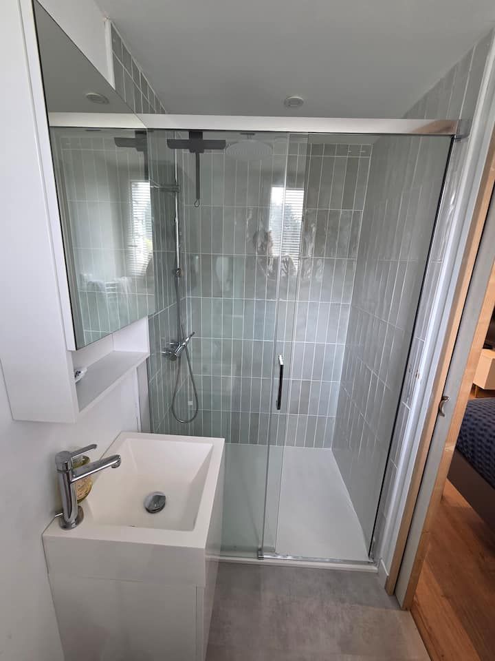Salle de bains moderne avec douche en verre, lavabo suspendu et murs carrelés gris clair